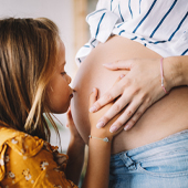 Kind küsst schwangeren Mutter auf den Bauch