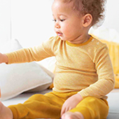 Baby sitzend mit gelber Kleidung aus Wolle/Seide
